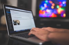 Les mains d'une personne utilisant un clavier d'ordinateur portable. À l'écran, un article de blog.